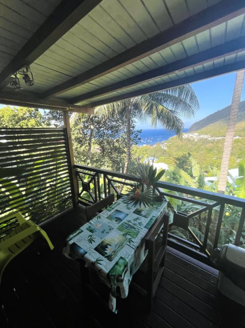 Terrasse couverte aux Hauts de Deshaies avec vue panoramique sur la baie de Deshaies et jardins tropicaux