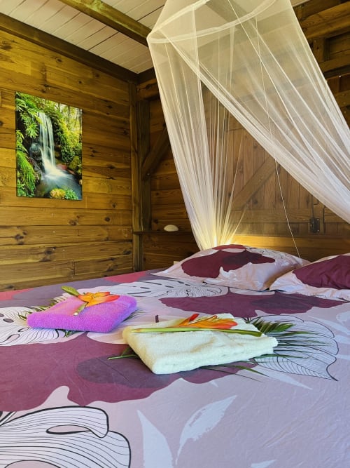 Chambre tropicale avec voile de baldaquin, literie colorée, tableau cascade et murs en bois aux Hauts de Deshaies
