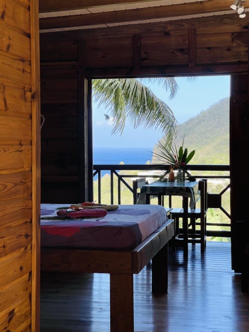 Chambre avec balcon vue mer aux Hauts de Deshaies, Guadeloupe, intérieur en bois et vue sur les montagnes