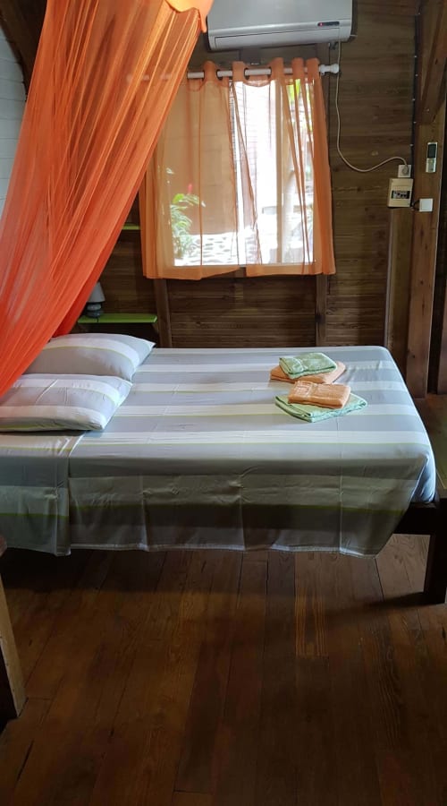 Chambre lumineuse aux Hauts De Deshaies avec lit blanc, rideaux orange et vue mer à Deshaies
