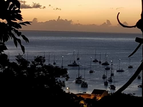 Vue du coucher de soleil sur la baie de Deshaies avec des voiliers ancrés, encadrée par une végétation tropicale