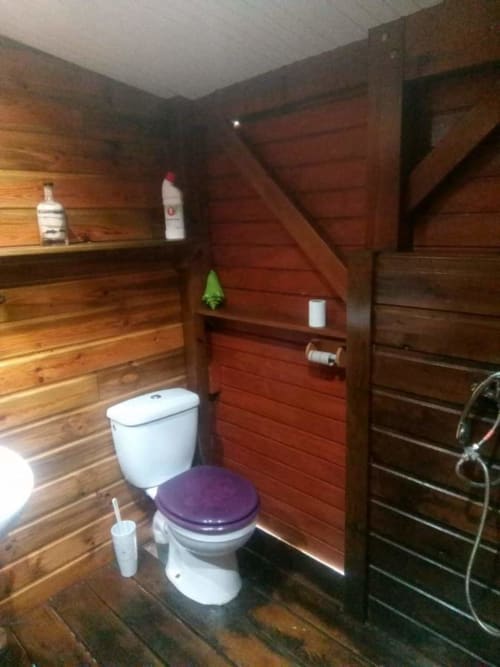Salle de bain en bois avec toilettes blanches et siège violet à l'appartement Les Hauts De Deshaies à Deshaies
