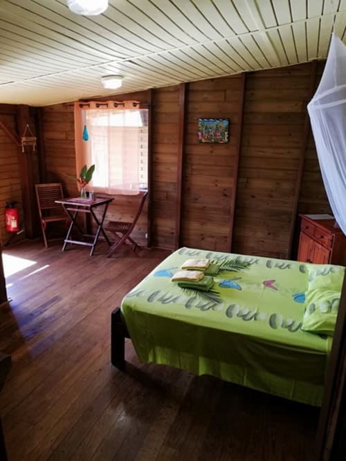 Chambre de cottage en bois aux Hauts de Deshaies avec literie verte, bureau et vue mer à Deshaies