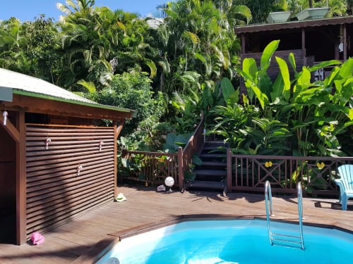Piscine de la villa tropicale Les Hauts De Deshaies avec palmiers luxuriants, terrasse en bois et eau turquoise à Deshaies