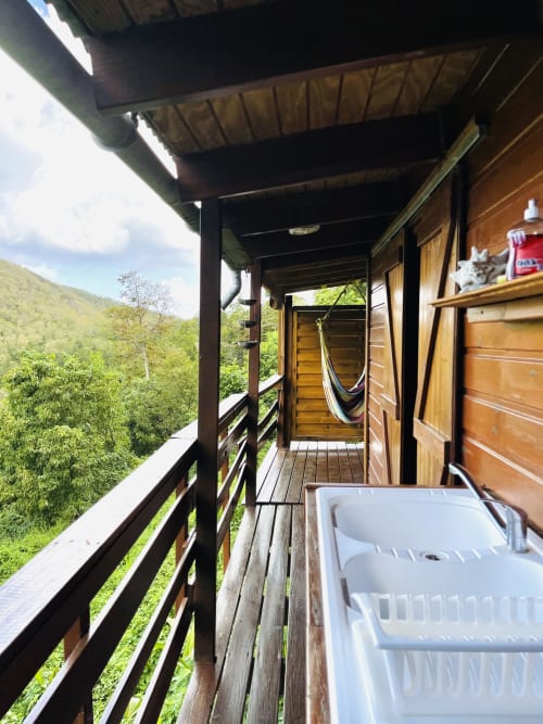 Terrasse en bois des Hauts de Deshaies avec vue panoramique sur la vallée luxuriante, évier, hamac et montagnes