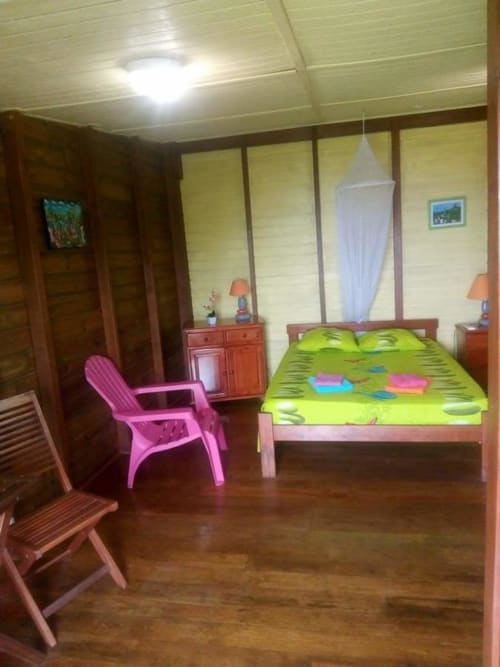 Chambre lumineuse aux Hauts de Deshaïes avec literie vert citron, fauteuil rose, mobilier en bois et vue sur la mer