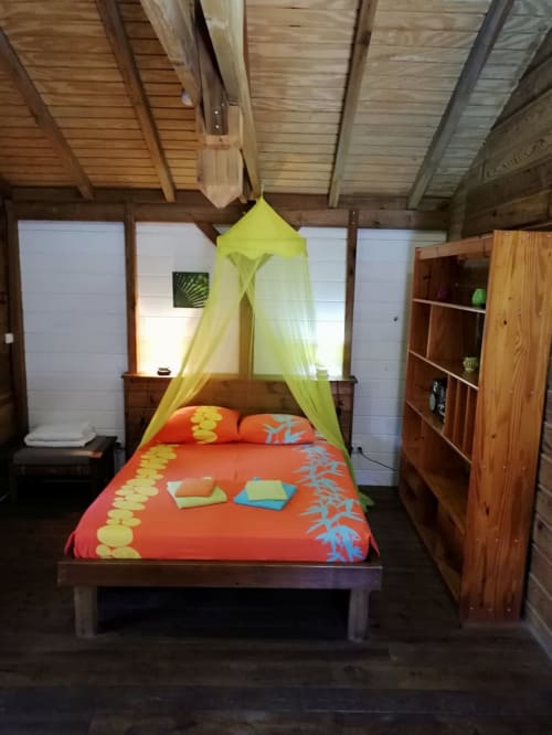 Chambre tropicale aux Hauts de Deshaïes avec lit à baldaquin en bois, moustiquaire jaune et literie orange vif