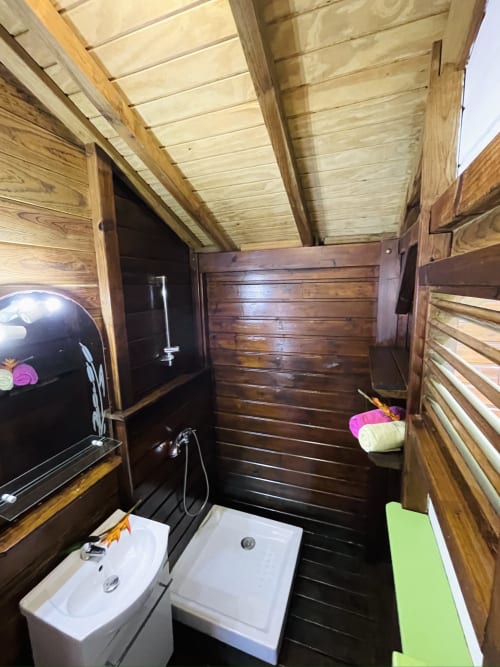 Salle de bain en bois avec vue sur mer aux Hauts de Deshaies, Guadeloupe, avec sanitaires blancs et bois naturel