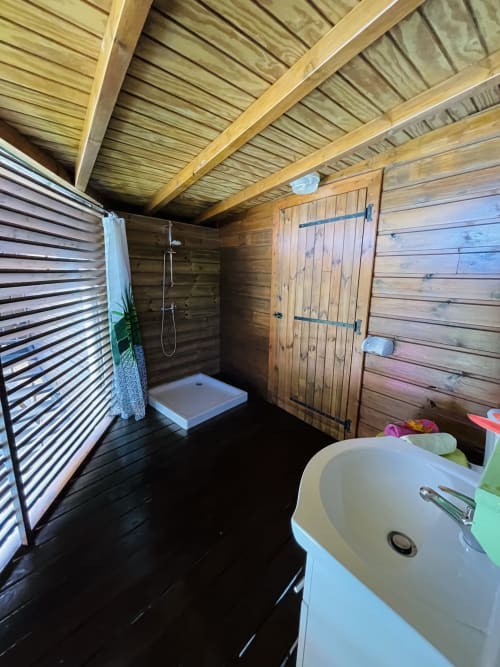 Salle de bain du cottage en bois avec lavabo, douche et sol noir aux Hauts de Deshaies