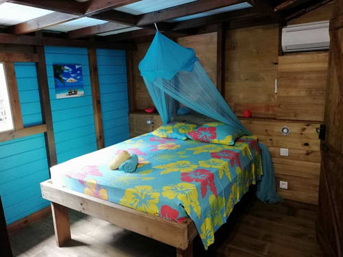 Chambre tropicale aux murs bleu vif aux Hauts De Deshaies avec parure fleurie colorée et baldaquin à Deshaies