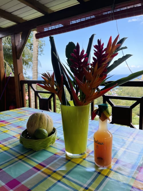 Table de patio colorée aux Hauts de Deshaies avec fleurs tropicales et vue sur l'océan à Deshaies