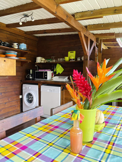 Cuisine de cottage colorée aux Hauts de Deshaies avec fleurs tropicales, nappe tartan arc-en-ciel et appareils modernes