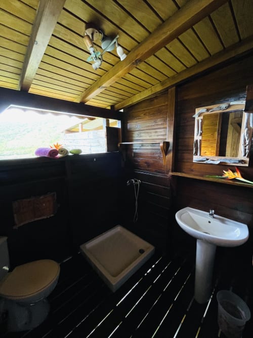 Salle de bains avec poutres en bois et fenêtre vue mer au gîte Les Hauts De Deshaies, Deshaies