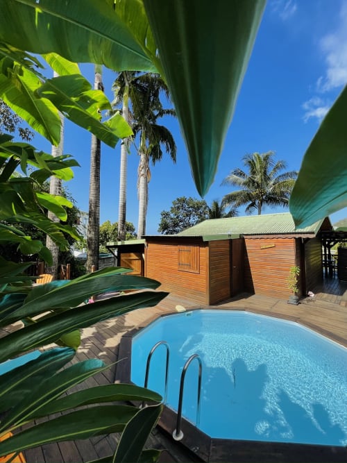 Piscine bleue entourée de plantes tropicales et de bungalows en bois aux Hauts de Deshaies, Guadeloupe