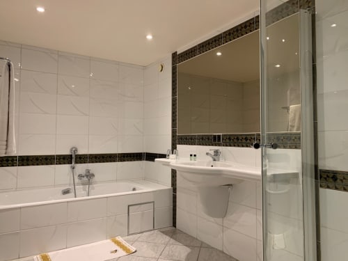 Modern bathroom at Le Moulin Des Ramiers with white tiles, dark trim, bathtub, sink, mirror, and walk-in shower
