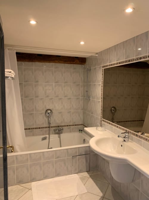 Modern bathroom at Le Moulin Des Ramiers with white sink, bathtub, tiled walls, and mirror in Crupet, Belgium