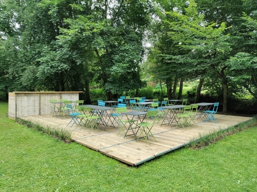 Terrasse en bois en plein air avec chaises et tables pliantes bleues à l'hôtel Le Moulin Des Ramiers à Crupet, entourée de verdure