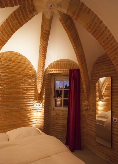 Camera da letto con volta in mattoni a La Tour Du Capitole, Toulouse: soffitti voltati, biancheria bianca, tenda rossa e illuminazione calda