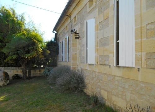 Façade en pierre du gîte Sous Les Marronniers à Petit Palais Cornemps, avec volets blancs et jardin méditerranéen
