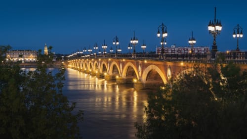 Pont de pierre illuminé enjambant la rivière au crépuscule près de Sous Les Marronniers à Petit Palais Cornemps, France
