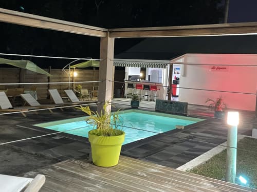 L'espace piscine du Kaz A Bibi la nuit, avec sa piscine turquoise illuminée, transats et bâtiment rose à Sainte-Rose