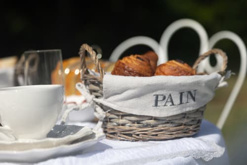 Table du petit-déjeuner au Manoir Le Coutureau avec panier de pain, tasse blanche et vue sur la campagne de Rouffignac de Sigoules