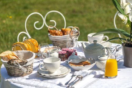 Table de petit-déjeuner élégante au Manoir Le Coutureau avec viennoiseries, jus frais, service de thé et jardin en arrière-plan