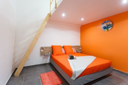 Chambre lumineuse aux teintes orangées à la villa Kaz A Bibi à Sainte-Rose, avec lit queen, équipements modernes et escalier vers mezzanine