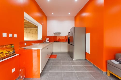 Cuisine orange vif à la villa Kaz A Bibi, Sainte-Rose, avec armoires blanches, électroménagers inox et carrelage gris