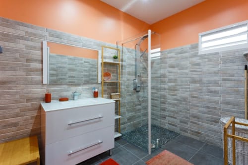 Salle de bain moderne aux murs orange, douche en carrelage gris, meuble lavabo blanc, avec vue sur le jardin à la villa Kaz A Bibi à Sainte-Rose