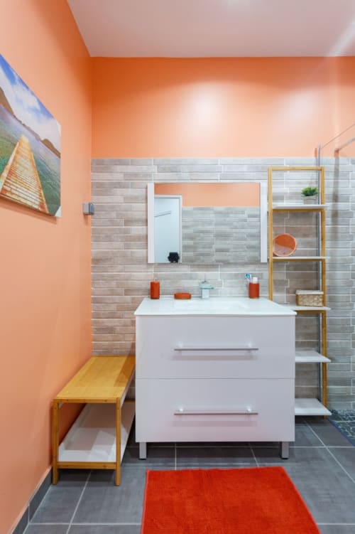Salle de bain moderne de la villa Kaz A Bibi à Sainte-Rose avec murs orange, lavabo blanc et carrelage gris