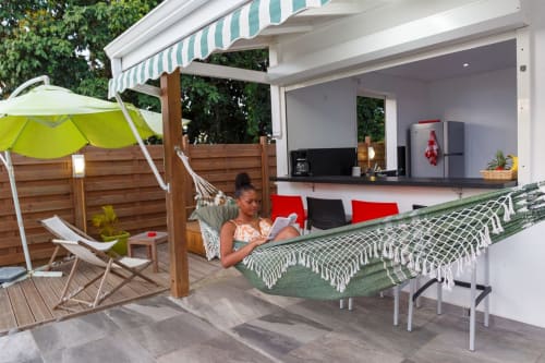 Femme se relaxant dans un hamac à la villa Kaz A Bibi avec vue sur la piscine, cuisine extérieure et auvent à rayures vertes à Sainte-Rose