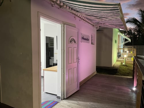 Façade rose de la maison d'hôtes Kaz A Bibi à Sainte-Rose, Guadeloupe, avec terrasse en bois et store rayé au crépuscule