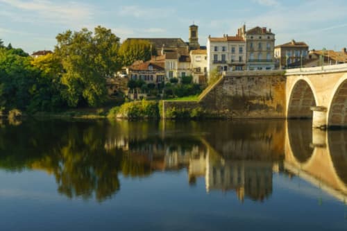Pont de pierre se reflétant dans une rivière calme avec des bâtiments villageois historiques et un clocher d'église, Rouffignac de Sigoules