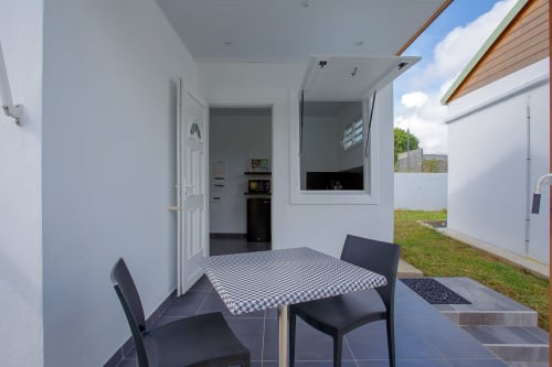 Salle à manger du cottage Kaz A Bibi à Sainte-Rose avec table à carreaux, chaises noires et accès à la vue piscine par portes ouvertes