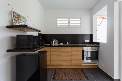 Kitchenette moderne du gîte Kaz A Bibi à Sainte-Rose avec meubles en bois, plan de travail noir et appareils en inox