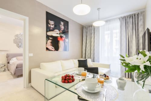 Moderno soggiorno dell'appartamento Petra Apartments Roma con divano color crema, tavolo in vetro, fiori freschi e vista della città dalle finestre