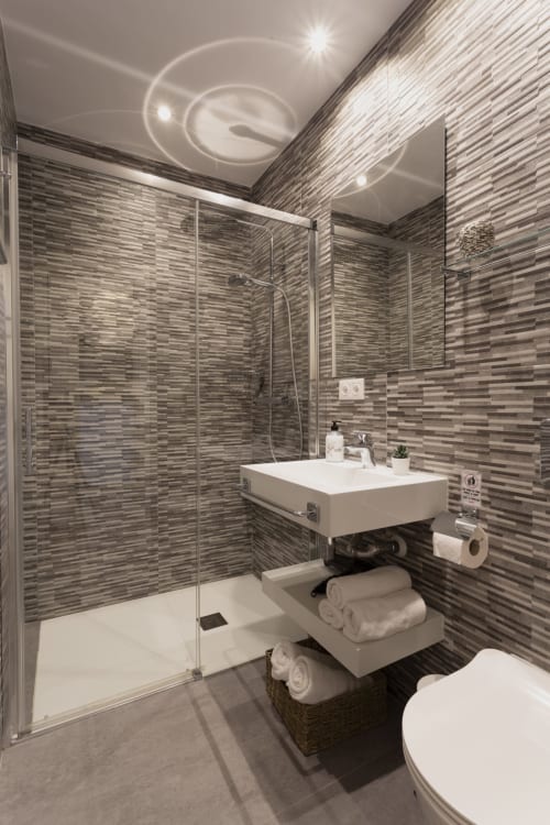 Baño moderno en Room Boutique 32 Denia con azulejos a rayas, cabina de ducha cristal, lavabo blanco y almacenamiento de toallas