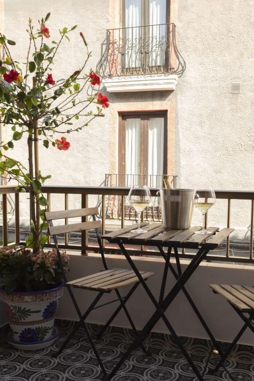 Balcón soleado en Room Boutique 32 Denia con mesa de comedor, copas de vino, flores rojas y vistas a la ciudad