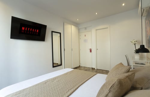 Dormitorio moderno en el hostal Room Boutique 32 de Denia con cama, TV montada en pared con Netflix, espejo y múltiples puertas