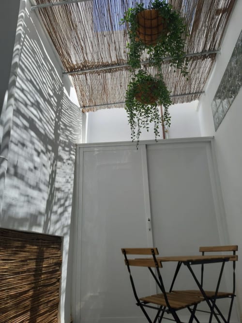 Habitación luminosa en Room Boutique 32 de Denia con plantas colgantes, muebles de madera y sombreado de techo tejido que crea luz natural