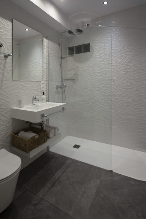 Baño moderno en la hostal Room Boutique 32 de Denia con azulejos blancos texturados, ducha a ras de suelo y accesorios elegantes
