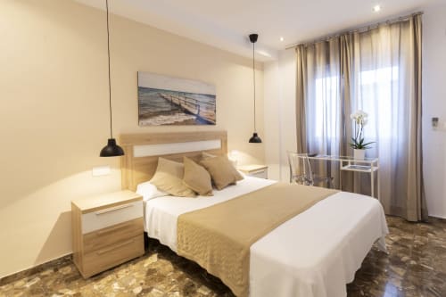 Dormitorio moderno en Room Boutique 32 hostel de Denia con cama de madera, ropa de cama beige, lámparas colgantes y acceso a balcón