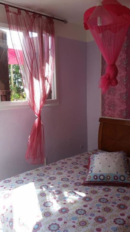 Chambre lumineuse à la Résidence Les 2 Moulins au Moule avec rideaux roses, literie patterned et lit en bois