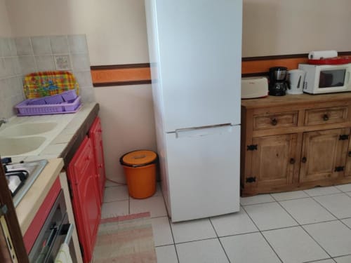 Cuisine de l'appartement Résidence Les 2 Moulins au Moule avec armoires rouges, réfrigérateur blanc et mobilier de salle à manger
