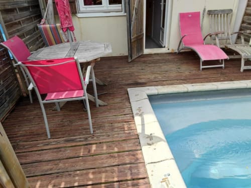 Espace piscine de la Résidence Les 2 Moulins avec transats roses sur terrasse en bois et piscine bleue