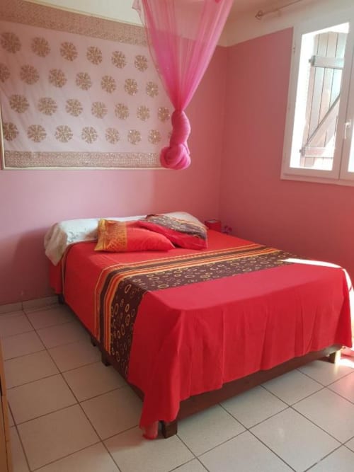 Chambre rose vif avec lit rouge et coussins décoratifsà la Résidence Les 2 Moulins, Le Moule, Guadeloupe