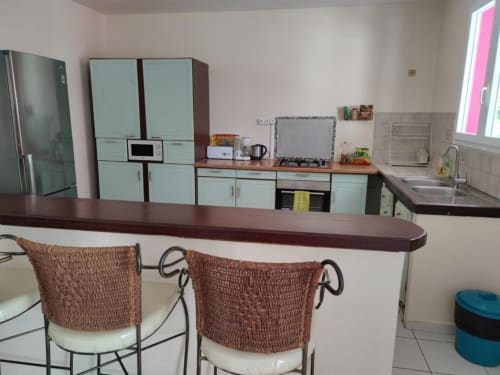 Cuisine moderne aux armoires vert menthe, îlot à comptoir sombre avec chaises tressées, électroménagers inox à Résidence Les 2