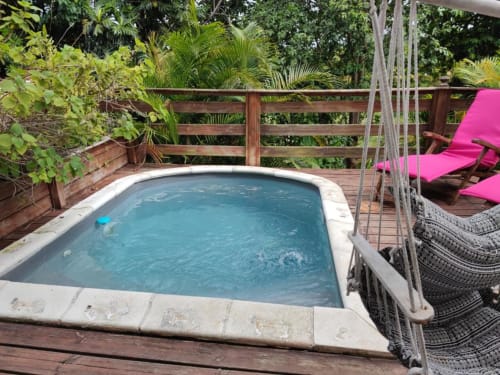 Bain à remous turquoise sur terrasse en bois avec chaises longues roses, plantes tropicales et rampes en bois à la Résidence Les 2 Moulins