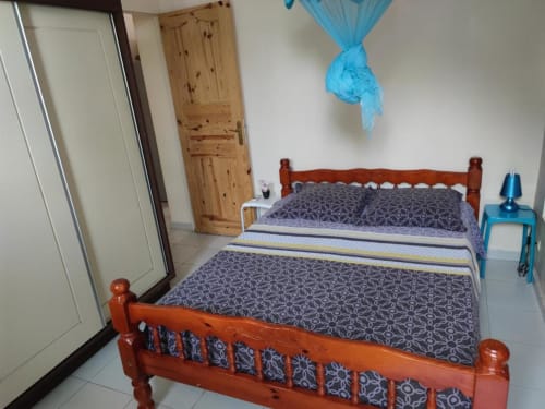 Chambre spacieuse avec lit en bois orange, linge de lit à motifs, lampe de chevet bleue et armoire en bois à la Résidence Les 2
